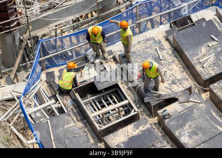 Group of construction workers wearing safety vests and helmets working on a building framework. Stock Photo