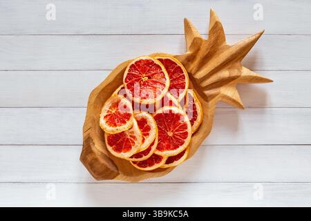 Dried grapefruit slices arranged in a wooden pineapple shaped bowl on a white wooden table surface Stock Photo