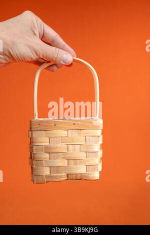 Hand Holds Miniature Woven Basket Against Orange Stock Photo