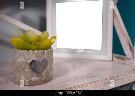 A decorative planter shaped like a heart holds vibrant green and yellow succulents. Nearby, a blank photo frame sits on a wooden shelf, enhancing the Stock Photo