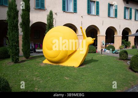 Large yellow snail sculpture on a lawn in Cannobio, Italy, part of a public art exhibition featuring colourful animal installations. Stock Photo