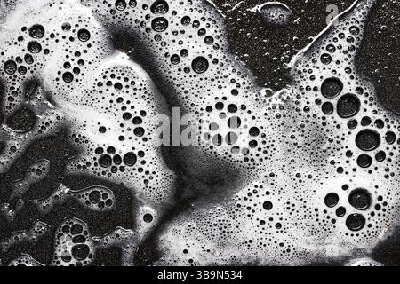 Soap foam abstract texture. White bubbles on black surface. Cleaning background macro. Washing product residue. Detergent pattern top view. Stock Photo