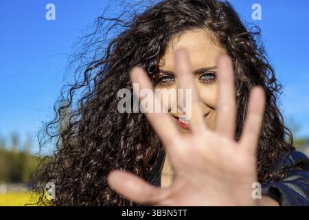 Portrait of a smiling blue-eyed young woman showing a stop sign while standing outdoors Stock Photo