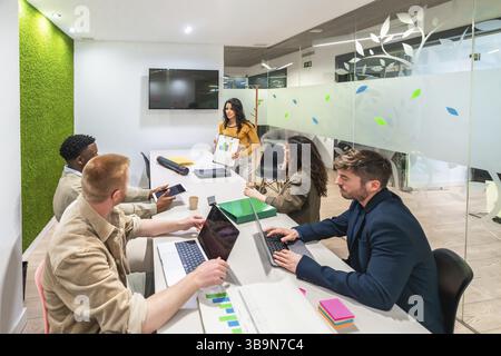 Marketing team working together in a modern office, using laptops and analyzing graphs during a productive meeting Stock Photo