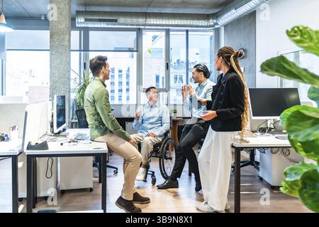 Businesspeople having a conversation in a modern office, demonstrating inclusion and teamwork with a colleague using a wheelchair Stock Photo