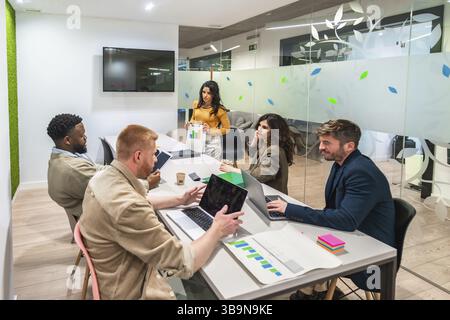Marketing managers collaborating on a project, analyzing charts and using laptops in a modern meeting room Stock Photo