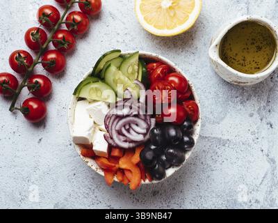 Greek Salad Bowl on gray cement background. Above view of Bowl Greek Salad with olive oil and ingredients. Trendy food. Idea, recept and concept of mo Stock Photo