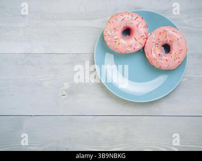 Top view of two pink donuts on gray wooden background with copy space. Colorful donuts on plate with copyspace. Glazed doughnuts with sprinkles on gre Stock Photo
