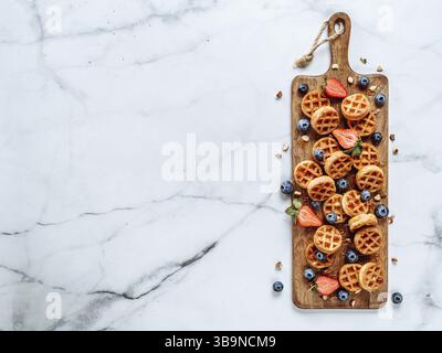 Small round delicious soft belgian waffles on cutting board. Fresh belgian waffles with berries and caramel sauce top view. Copy space for text or moc Stock Photo