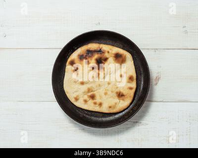 Fresh naan bread in cast-iron pan on white wooden background with copy space. Top view of perfect naan flatbread black circle cast iron pan Stock Photo