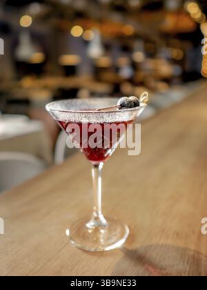 Red cocktail in martini glass on bar counter. Cranberry alcohol cocktail decorated white powdered sugar and black olive. Decorate cold alcoholic cockt Stock Photo