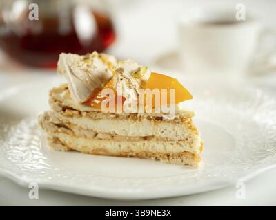 Puff layered cake with cream of cream-cheese, decorated fresh persimmons. Delicious and eye-catching piece of layered cake decorated crispy meringue a Stock Photo