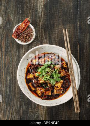 Spicy asian tofu salad or appetizer. Fried tofu decorated green onion - chinese dish with sauce. Serving Asian dish on brown wooden tabletop. Top view Stock Photo