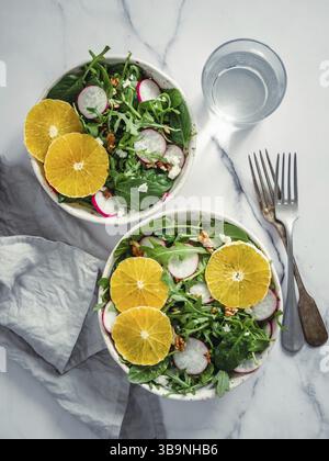 Vegan salad bowl with oranges, spinach, arugula, radish, nut. Top view. Vegan breakfast, vegetarian food, diet concept. Two bowls with salad on white Stock Photo