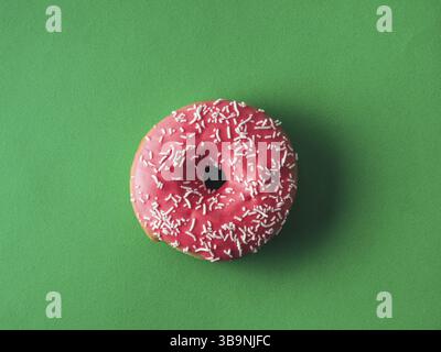Top view of pink glazed donut on green background. Glazed and topping sprinkle pink doughnut on rich green background. Top view or flat lay Stock Photo