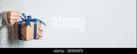 Female hands opening gift box on white background, copy space right.Unrecognizable caucasian girl in gray sweater holding gift box in craft wrapping p Stock Photo