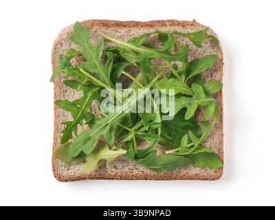 Bread slice with arugula leaves isolated on white, clipping path. Slice of multigrain bread square form with green arugula leaves for toast. Image of Stock Photo