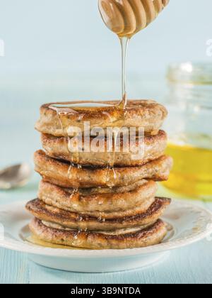 Stack of small pancakes with banana and chia seeds in honey on light blue background. Honey pouring over stack of mini pancakes with chia or poppy see Stock Photo