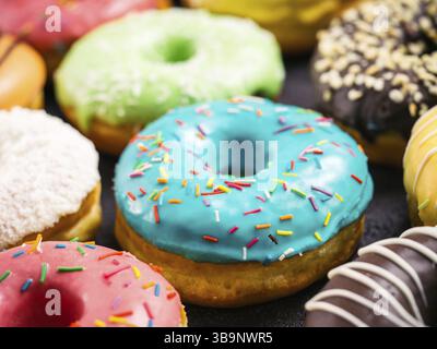 Close up view of assorted colorful donuts on dark background. Focus on blue glazed doughnut with sprinkles. Shallow DOF Stock Photo