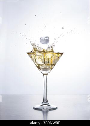 Yellow cocktail in martini glass with ice cube splashing into liquid against white background. Martini cocktail with splash on white background Stock Photo