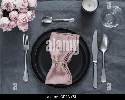 Beautiful table setting with pink spray roses and candle on gray linen tablecloth. Festive table setting for wedding dinner with pink napkin on plate. Stock Photo