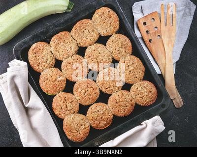 Top view of baking tray with homemade vegetables muffins. Cupkace with zucchini, carrots, apple and cinnamon on black cement background. Sweet vegetab Stock Photo
