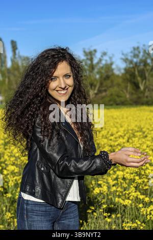 Vertical portrait of a beautiful young woman smiling looking at camera with yellow flower petals in her hand Stock Photo