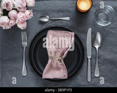 Beautiful table setting with pink spray roses and candle on gray linen tablecloth. Festive table setting for wedding dinner with pink napkin on plate. Stock Photo
