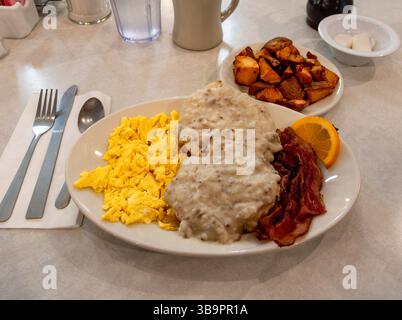 A mouthwatering classic diner breakfast: two fluffy scrambled eggs, crispy bacon, two buttery biscuits drenched in creamy sausage gravy, warm golden h Stock Photo