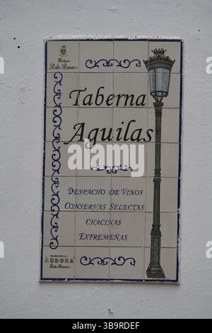 Ceramic tile sign for “Taberna Aguilas” on a white wall in Seville, Spain, advertising traditional wines, tapas-style products and local cuisine. Stock Photo