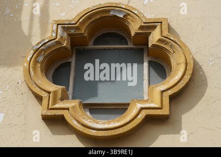 Detail of an ornate quatrefoil-shaped window frame on a historic facade in Seville, Spain, featuring warm tones and weathered plaster texture. Stock Photo