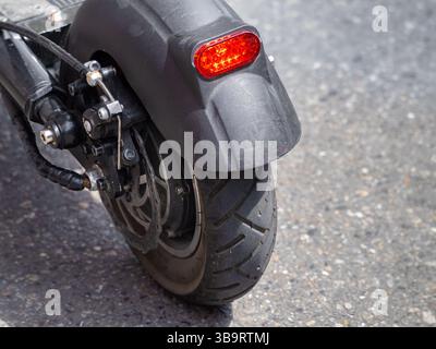 Close-up of a motorcycle rear wheel and brake light on a textured asphalt surface. Stock Photo