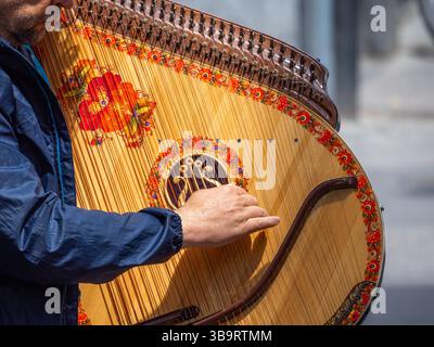 Bern, Switzerland - May 8, 2025: A musician playing a beautifully decorated wooden harp, showcasing intricate floral designs. The focus is on the play Stock Photo