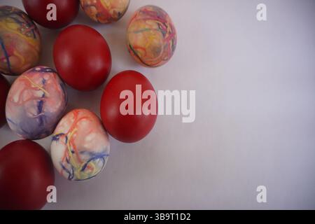Red Easter eggs and colorful eggs dyed with thread dipped in various colors scattered on one side Stock Photo