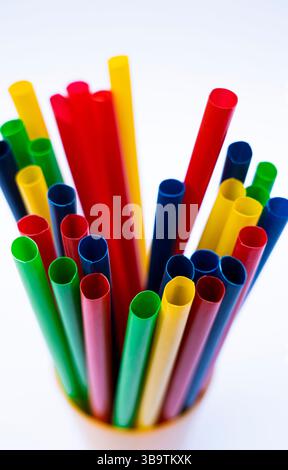 Closeup of Colorful plastic straws standing upright in cup on white background Stock Photo