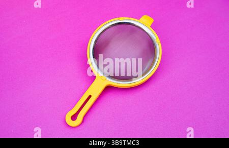 A yellow tea or kitchen strainer with fine mesh placed on a bright pink background, isolated and shot from above. Stock Photo