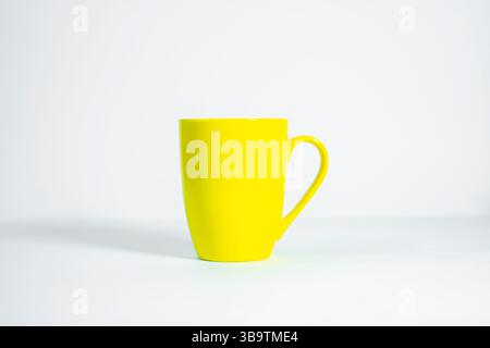 Simple yellow ceramic mug with handle, isolated on smooth white background. Stock Photo
