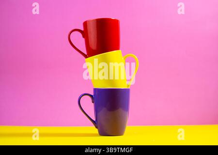 Modern stacked cups in various colors placed on bold yellow and pink background. Stock Photo