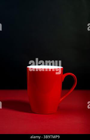 Vibrant Red ceramic mug with curved handle on Red and Black background. Stock Photo