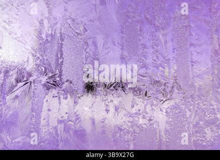 Frosty textures of ice crystals on clear window glass. Frozen surface, snowflake texture on lilac tinted glass. Stock Photo
