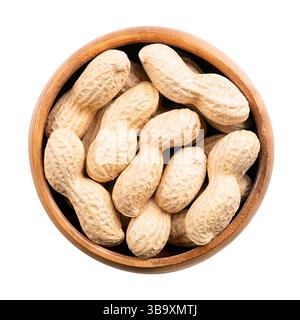 In-shell roasted peanuts in a wooden bowl. Whole, crunchy nut, fruits of Arachis hypogaea, encased in its natural shell. Light golden snack food. Stock Photo