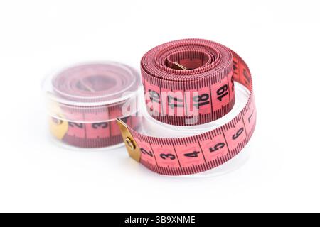 Tailor measuring tape closeup. Pink flexible ruler rolled in spiral. Centimeter scale for sewing or body measurement. Tailoring tool on white. Stock Photo