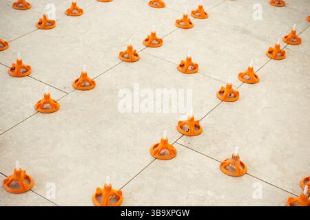 Close-up view of ceramic floor tiles being installed using a professional tile leveling system with orange wedges and spacers Stock Photo