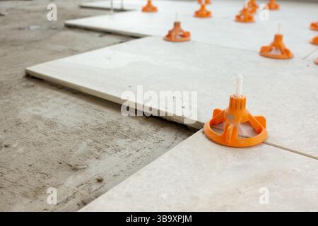 Close-up view of ceramic floor tiles being installed using a professional tile leveling system with orange wedges and spacers Stock Photo