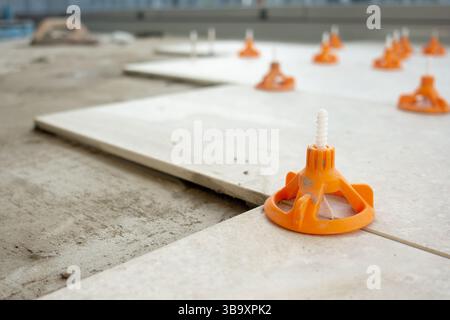 Close-up view of ceramic floor tiles being installed using a professional tile leveling system with orange wedges and spacers Stock Photo