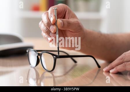 Close up of man hands tightening screw on glasses with screwdriver on a desk at home.Male optician repairing and fixing eye glasses with screwdriver. Stock Photo