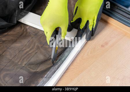 Close-up of a man's hands installing a wire mosquito net on a window in his house to protect from insects.Mosquito net windows Stock Photo