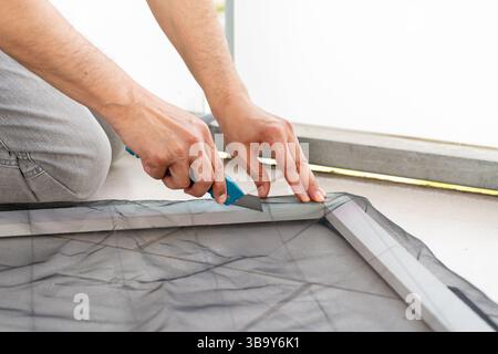 Close-up of a man's hands installing a wire mosquito net on a door in his house to protect from insects.Mosquito net windows Stock Photo