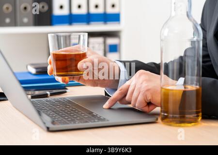 Close up of entrepreneur man hands drinking alcohol working on laptop sitting on a desk at home office Stock Photo