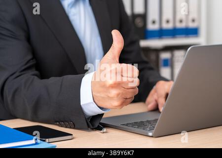Businessman hand with thumbs up using laptop at office Stock Photo